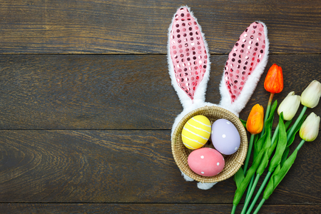 Top view shot of arrangement decoration Happy Easter holiday background concept.Flat lay colorful Easter egg with tulip flower and bunny ear on modern brown wooden at office desk.space for mock upの写真素材