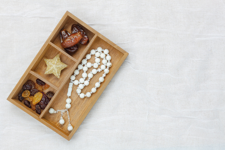 Table top view aerial image of decoration Ramadan Kareem holiday background.Flat lay date with white rosary & grape dried in brown wood shelf.Essential objects on modern rustic cloth at office desk.の写真素材