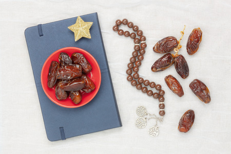 Table top view aerial image of decoration Ramadan Kareem holiday background.Flat lay date in plate with brown rosary & the holy book of Koran on modern rustic white clothing at office desk.food set.の写真素材