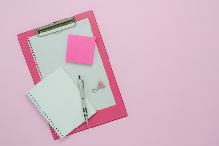 Table top view aerial image of back to school of education season background concept.Flat lay paper clip board with note nook and pen on modern rustic pink paper.Free space for creative design text.の写真素材
