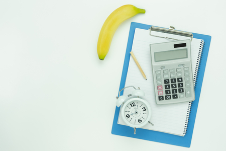 Table top view aerial image of count cal weight for sport fitness background concept.Flat lay essential objects notebook & pen with banana on modern rustic white wooden office desk background.の写真素材