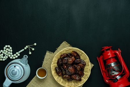 Table top view aerial image of decoration Ramadan Kareem holiday background.Flat lay date with rosary & lighting and cup of tea.Essential object on modern rustic black wooden at office desk.copy spaceの写真素材
