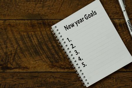 Table top view aerial image of 2020 new year business  goals & plans concept.Flat lay of essential object on brown wood.Text on notepad with black coffee and pen for accessories office desk backdropの写真素材