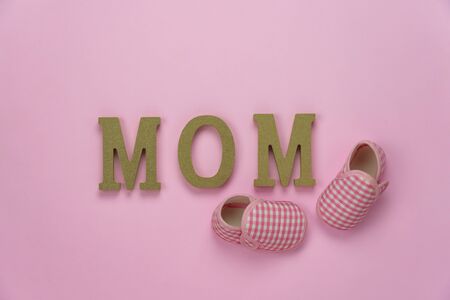 Top view aerial image of decoration Happy mothers day holiday background concept.Flat lay baby shoes and MOM text on modern beautiful pink paper at home office desk.pastel tone creative design.の写真素材