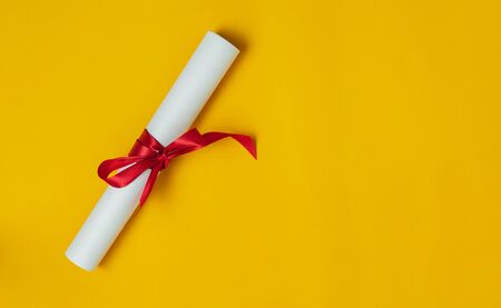 Table top view aerial image of Graduation of education season background concept.Flat lay accessories certificate document and red ribbon on modern rustic yellow paper.Free space for creative design.の写真素材