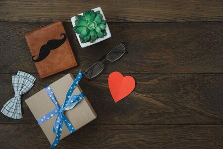 Table top view Happy Fathers day holiday on office desk background concept.Flat lay gift box for dad with objects the bow tie,tree pot,wallet,mustache,love heart paper,eyeglasses on brown wooen .の写真素材