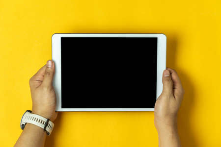 Table top view aerial image of accessories office desk background concept.Flat lay of Hand holding on white tablet on modern rustic yellow paper and space.の写真素材