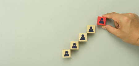 Top view of human resources and recruiting business or team leader management concepts. Hand adult Asian man holding difference of people icon on  wooden block. Objects on grey paper background.の写真素材