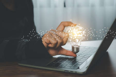 Hand man holding of light bulb with business and finance icon. Using laptop online technology working. Creative ideas. New idea, Creativity innovation and solution concepts. Human Inspiration .の写真素材