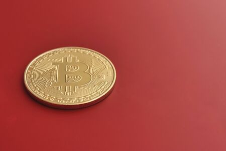 gold metal Bitcoin resting on a red background
