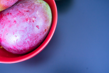 Fresh red mango in red bowl with drops of waterの写真素材