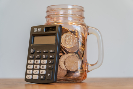 Black Pocket Calculator beside mason jar full of coinsの写真素材