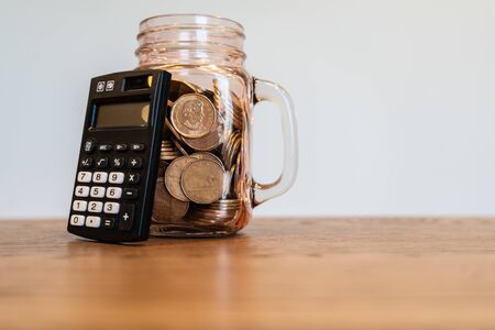 Black Pocket Calculator beside mason jar full of coinsの写真素材