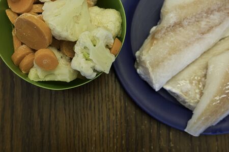 Fish and vegetables defrosting on table in kitchen