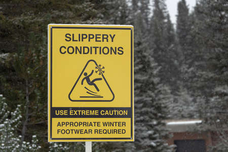 Slippery conditions warning sign in national park during snowfallの写真素材