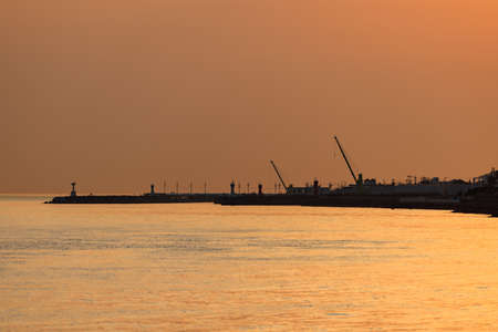 Orange haze over silhouetted cranes and pier on dockの写真素材