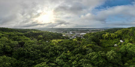 Panorama with small Japanese village surrounded by green hills under early morning sun