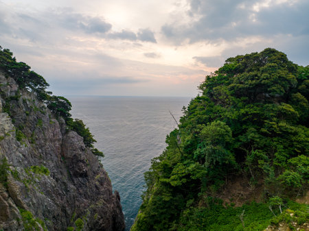 Opening between rugged coastal cliffs reveals morning sunrise on calm seaの写真素材