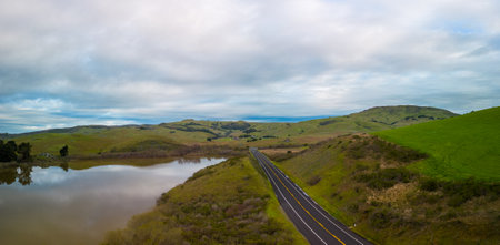 Empty road by green hills and reservoir in beautiful California at dawnの写真素材