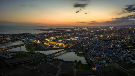Train tracks over pond with sunset glow in sky as city lights up at duskの写真素材
