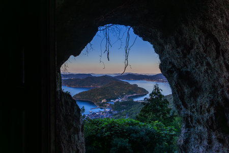 Shodoshima, Japan - September 25, 2023: Arched natural cave view to small coastal town and islands at sunriseのeditorial素材
