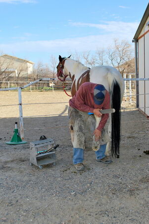 Male farrier working on a horseshoe outside の写真素材