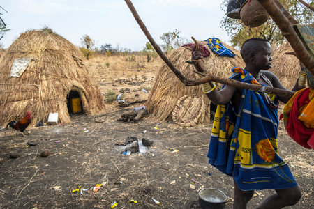 Omorate, Ethiopia - January 24: Unidentified woman from Mursi tribe posing for a portrait next to a tree with the traditional houses of the Mursi in the background on January 24, 2018 in Ethiopia.のeditorial素材