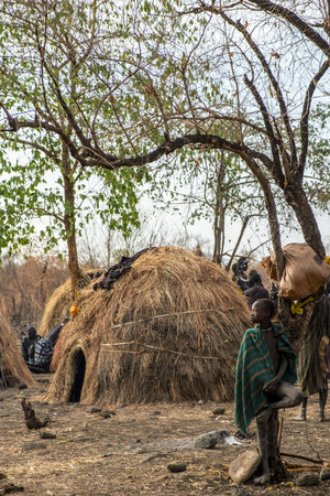 Omorate Ethiopia - January 24: Unidentified child from Mursi tribe posing for a portrait in his village with the traditional houses of the Mursi in the background on January 24, 2018 in Ethiopia.のeditorial素材