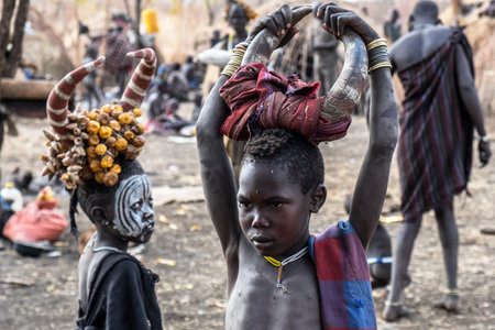 Omorate Ethiopia - January 24: Unidentified child from Mursi tribe posing for a portrait in his village with the traditional houses of the Mursi in the background on January 24, 2018 in Ethiopia.のeditorial素材