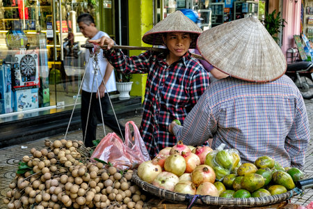 Hanoi, Vietnam - August 31: Street vendor carrying vegetables and fruit in baskets using a carrying pole on August 31, 2018 in Hanoi, Vietnam.のeditorial素材