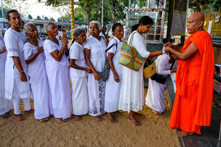 Kataragama, Sri Lanka - January 2020: A row of women receiving a bracelet from a monk at the Maha Devale Hindu sanctuary on January 18, 2020 in Kataragama, Sri Lanka.のeditorial素材