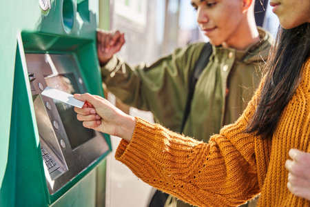 Tourists getting public transport tickets at a machine at a tram stop. young couple of male and female taking cash money from the bank atm machine.の写真素材