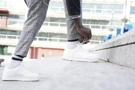 detail of young hipster in blazer and sneakers lacing up outdoors in townの写真素材