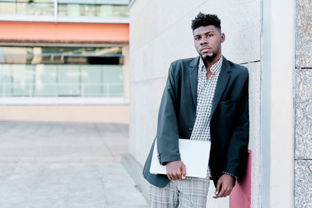 african-american businessman leaning against a wall with a laptop computer. copy space for text.の写真素材