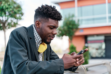Outdoor portrait of a young black African-American man talking on his mobile phone, writing on his smartphone in the city. social networking conceptの写真素材