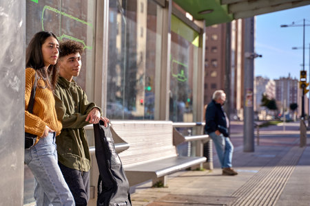 Youth teenagers people waiting for transportation on tram or bus stop. Brunette latin woman and hipster student man. concept of transport.の写真素材