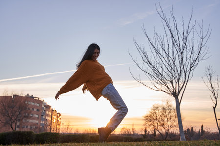 portrait of a woman with her body bent on her toes in a park at sunsetの写真素材
