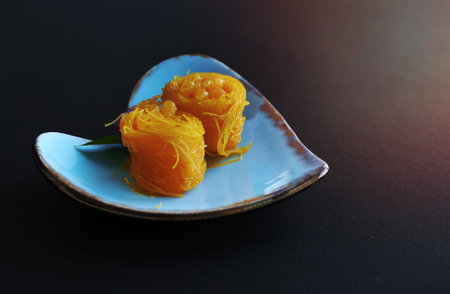 Close up of Thai style Fios de ovos, rolled golden egg yolk thread, traditional sweet food dessert in blue heart shape plate, with copy spaceの写真素材