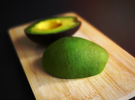close-up half cut vibrant color of fresh avocados beautiful green skin on wooden cutting boardの写真素材