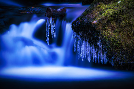 A small waterfall where a stick sticks out from which icicles hangの写真素材