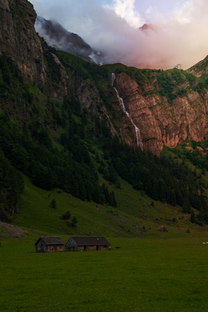 two farmhouses between mountains in the background a waterfallの写真素材