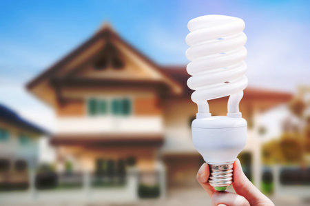 Energy saving concept, Woman hand holding light bulb on house background,Ideas light bulb in the...