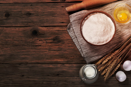 Flour, milk, eggs, ears of wheat in the bakery on wooden table. Top view with copy space. Baking...