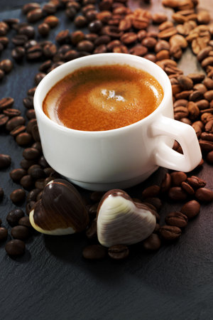 cup of espresso, coffee beans background and chocolate candies in a heart shape, vertical, close-upの写真素材
