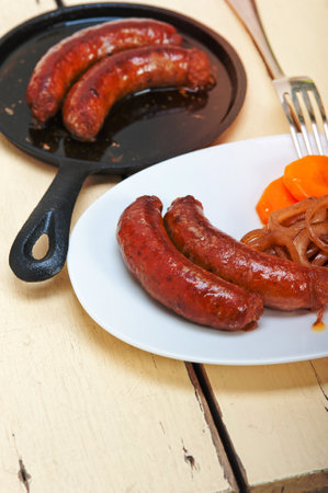 beef sausages cooked on iron skillet with carrot and onionの写真素材