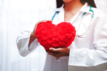 A beautiful Asian woman doctor holding a big red heart. In the treatment room. Hospital patient care conceptsの写真素材