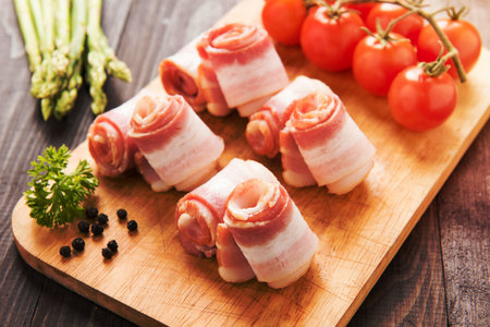 Bacon rolls with tomato, asparagus on wooden background.の写真素材