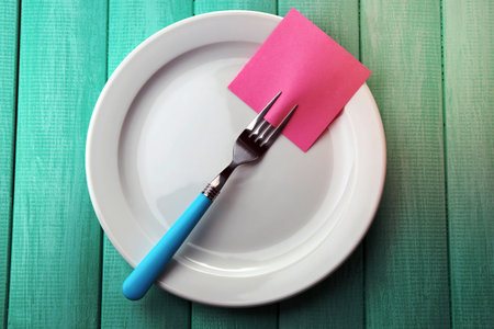 Empty note paper attached to fork, on plate, on color wooden backgroundの写真素材
