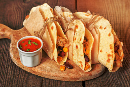 Mexican tortillas with chicken, cheese, corn, red beans and sauce on a wooden surfaceの写真素材