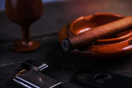 Cuban cigar in ashtray with lighter and cutter on rustic tableの写真素材